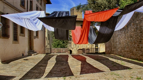 Immagine con nero, ombre, rosso, bianco, finestre, casa, panni, muro, cielo, alberi, teli, torre, verde, tende, colori, porte, porta, corde, azzurro, scalini, stesi, bucato, inferriate